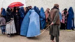 Співробітник служби безпеки «Талібан» стоїть на варті, поки афганські жінки в паранджі чекають у черзі посеред зливи, щоб отримати продукти харчування, пожертвувані під час священного місяця посту Рамадан. Кабул, Афганістан. 25 березня 2025 року